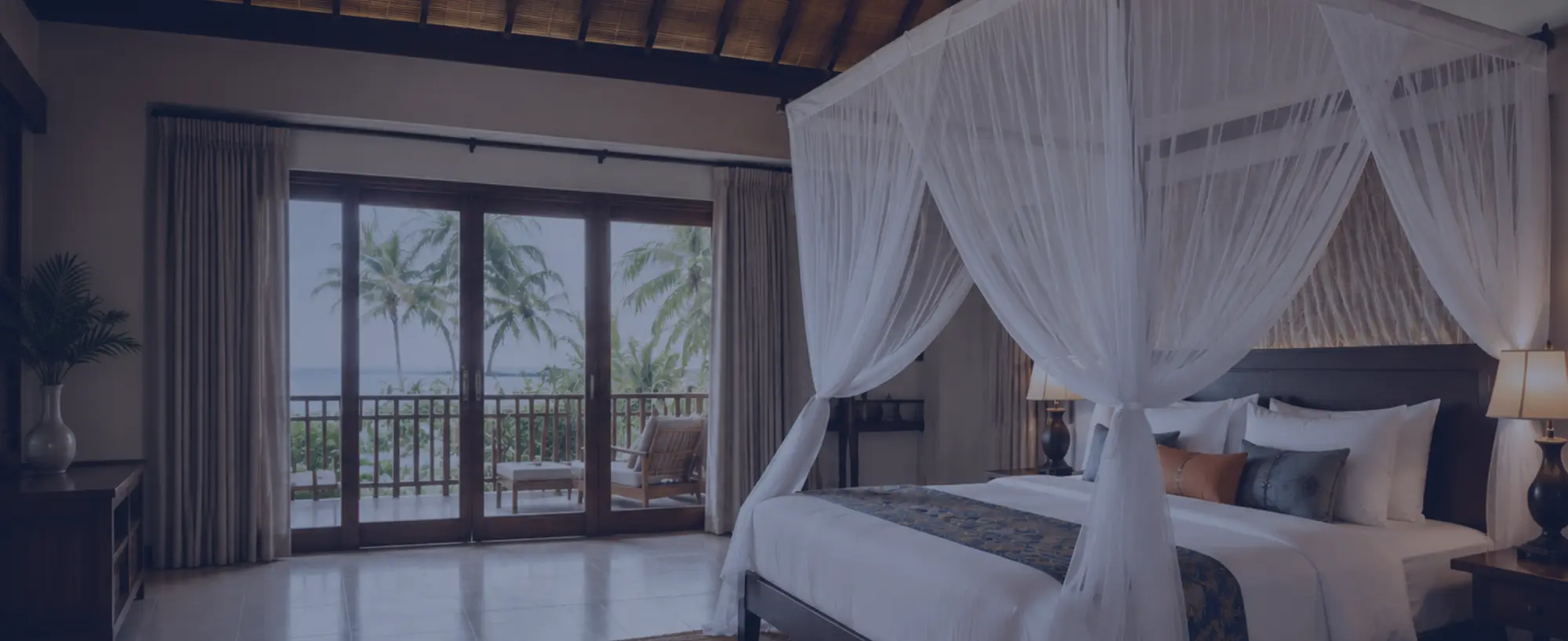 A canopy mosquito net over a bed in a Sri Lankan resort room opening onto the sea