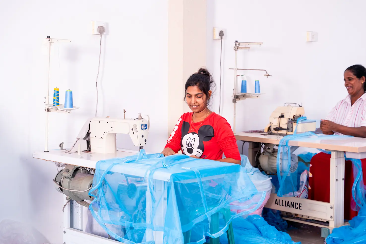 A machinist guiding a blue mosquito net through her sewing machine